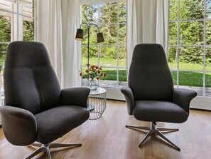Zwei moderne Sessel mit Metallbeinen, ein kleiner runder Tisch mit Blumenvase und ein Fenster mit Blick auf Grünflächen.