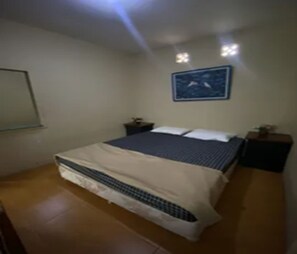 A bedroom with a bed, two bedside tables, a nightstand, a wall-mounted picture, and a tiled floor. - Cozzy Pondok Sukamulus (Bandung Barat)