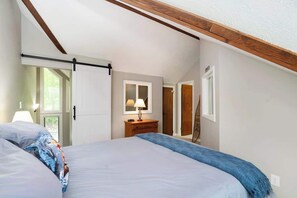 Ein Schlafzimmer mit Bett, Nachttisch, Lampe, Schiebetür und Fenster.