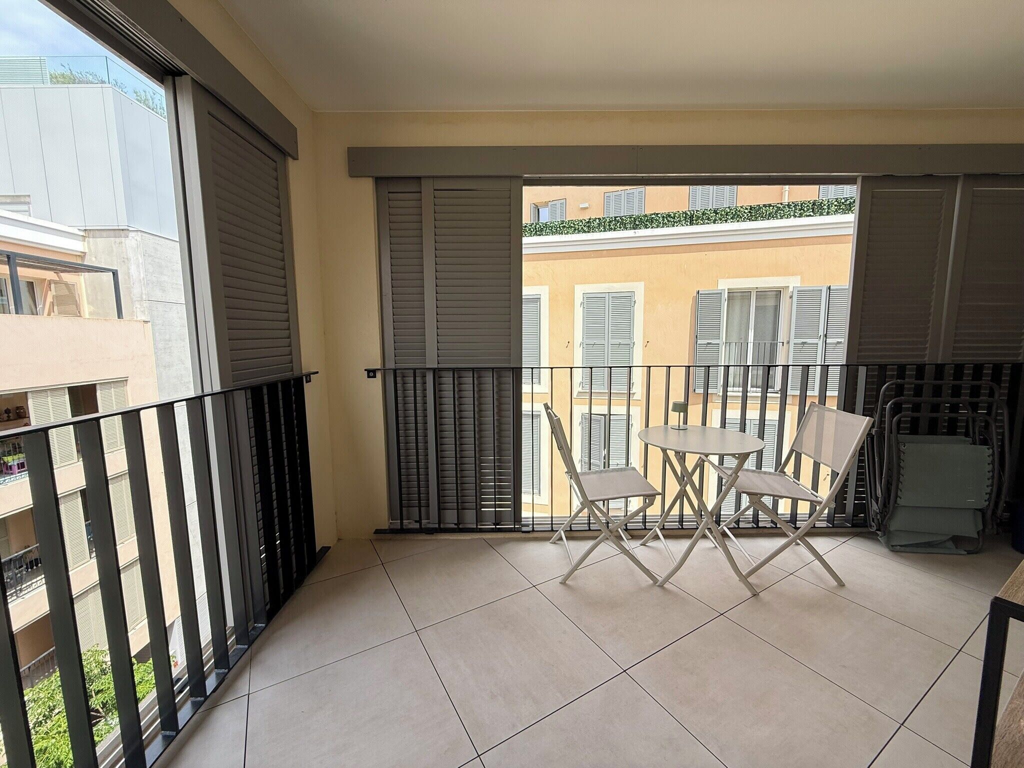 Een balkon met betegelde vloer, een kleine tafel met twee stoelen, en uitzicht op omliggende gebouwen.