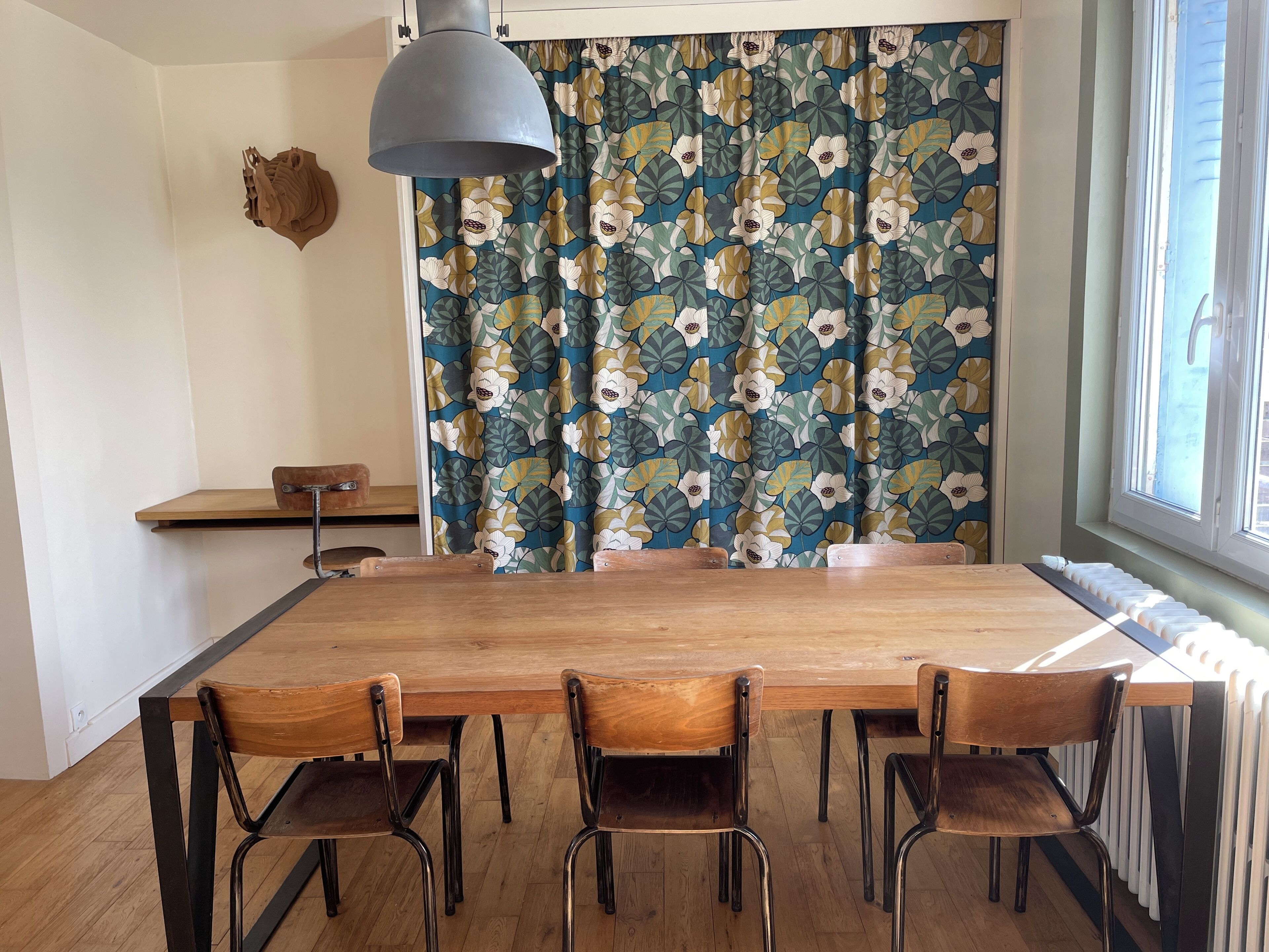 Un coin repas avec une table en bois, quatre chaises, un luminaire suspendu et une fenêtre donnant sur un beau paysage.