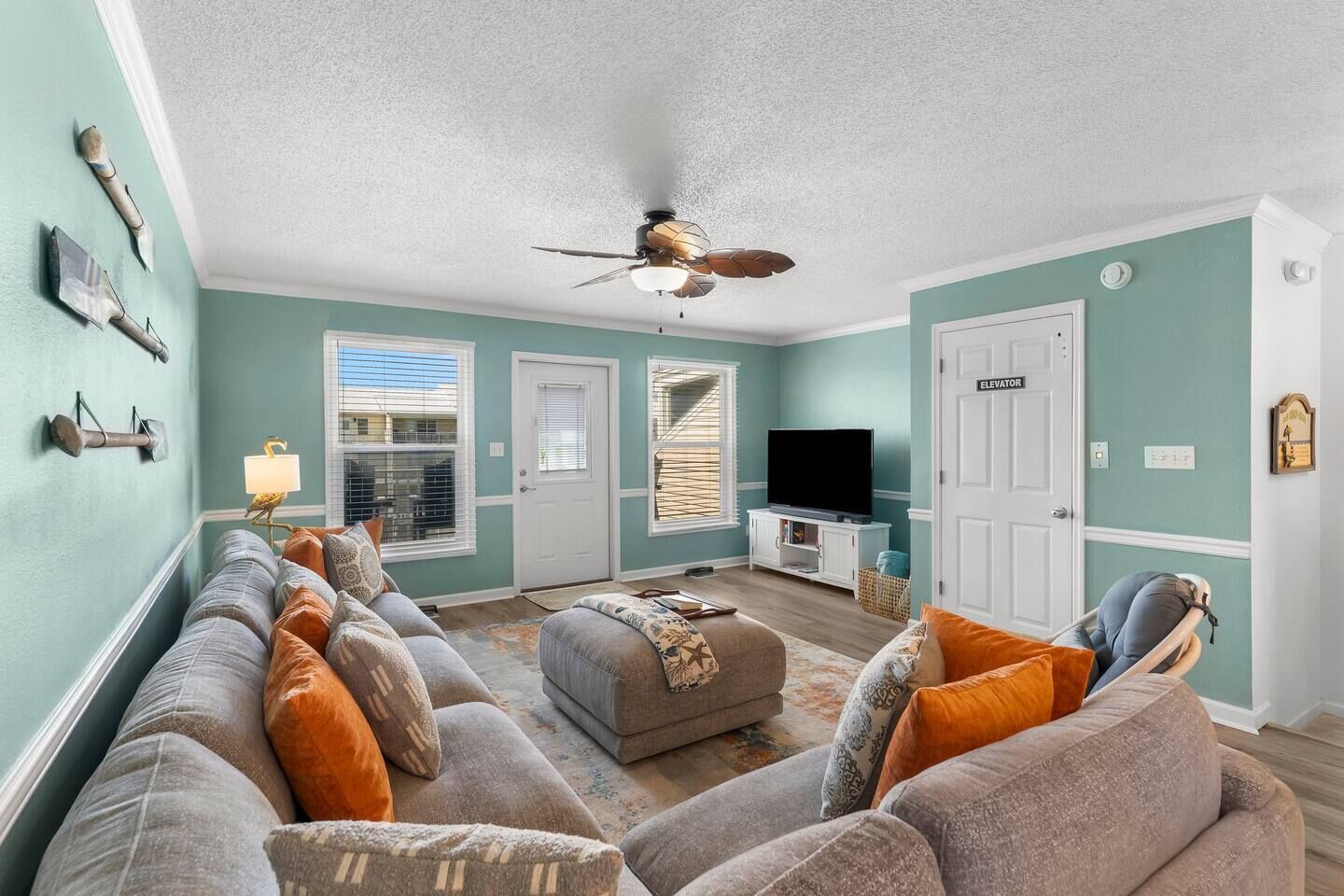 A living room with a sofa set, a television, a ceiling fan, and a door labeled 'Elevator'.