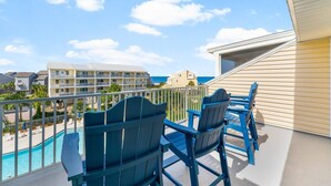 A balcony with blue Adirondack chairs, a pool, and a view of a hotel building and ocean. - The Mystic Turtle at Cape San Blas (Port St. Joe)