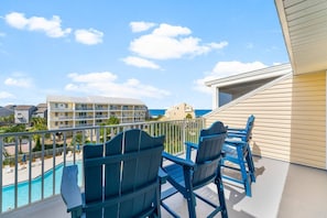 Ein Balkon mit blauen Adirondack-Stühlen, einem Pool und Blick auf ein Hotelgebäude sowie den Ozean.