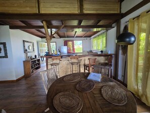 A rustic dining area with a wooden table, woven placemats, and a view of the kitchen.