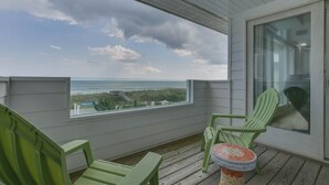 Un balcon avec vue sur l’océan, des chaises vertes et une petite table.