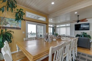 A dining area with a wooden table, white chairs, a ceiling fan, and a television on the wall. - Oceanfront Beach House with Pool, Hot Tub and Dune Deck 
Virginia Beach (Virginia Beach)