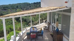 A covered patio with a table and chairs, a wooden cabinet, and a view of a hilly landscape. - Trullo in panoramic position near Ostuni (Ostuni)