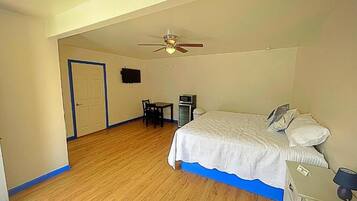 A bedroom with a bed, a desk, a chair, a ceiling fan, and a television.