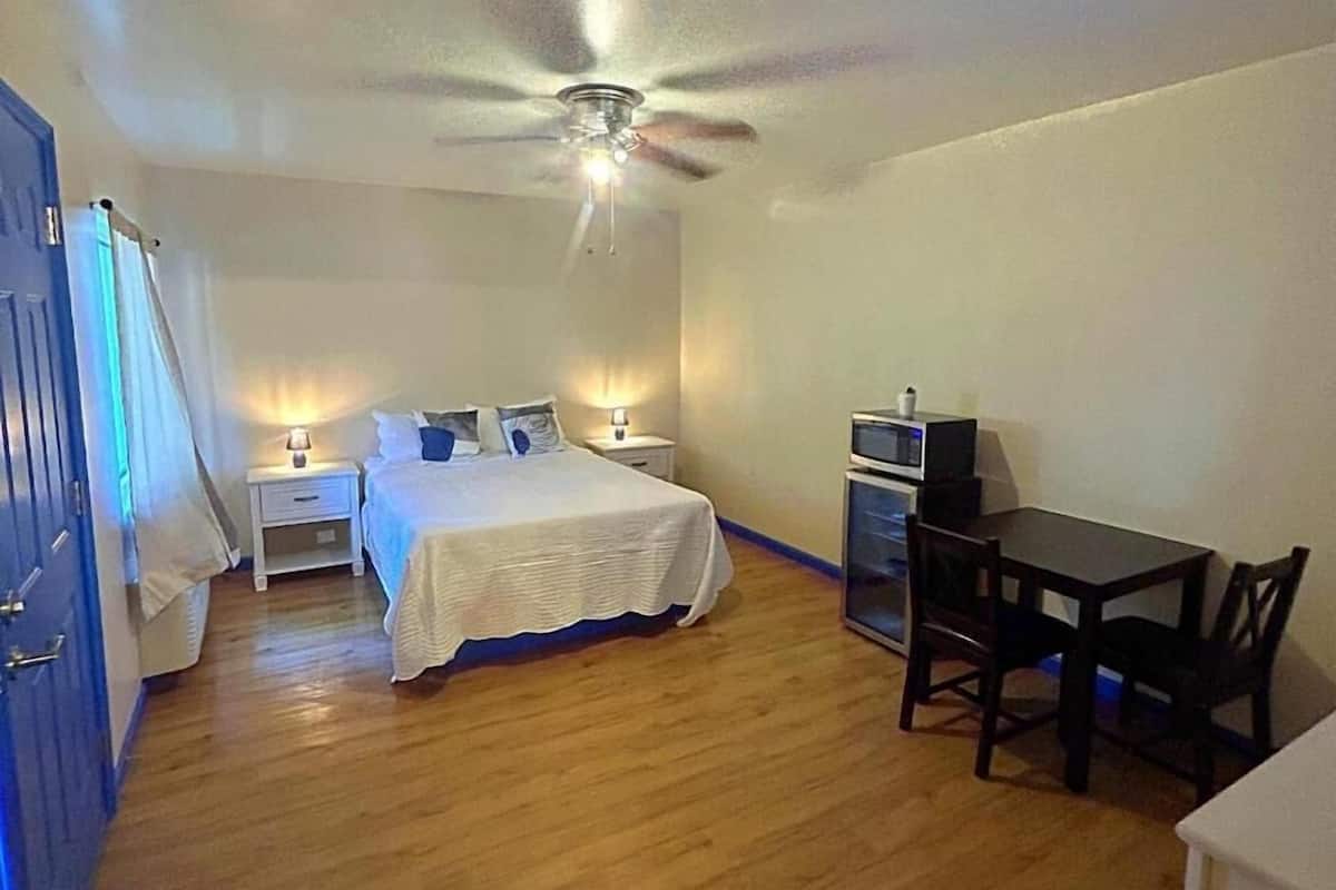 Un dormitorio con cama, mesitas de noche, ventilador de techo, televisión y una mesa de comedor con sillas.