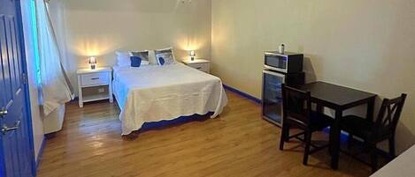 Een slaapkamer met een bed, nachtkastjes, een plafondventilator, een televisie en een eettafel met stoelen.