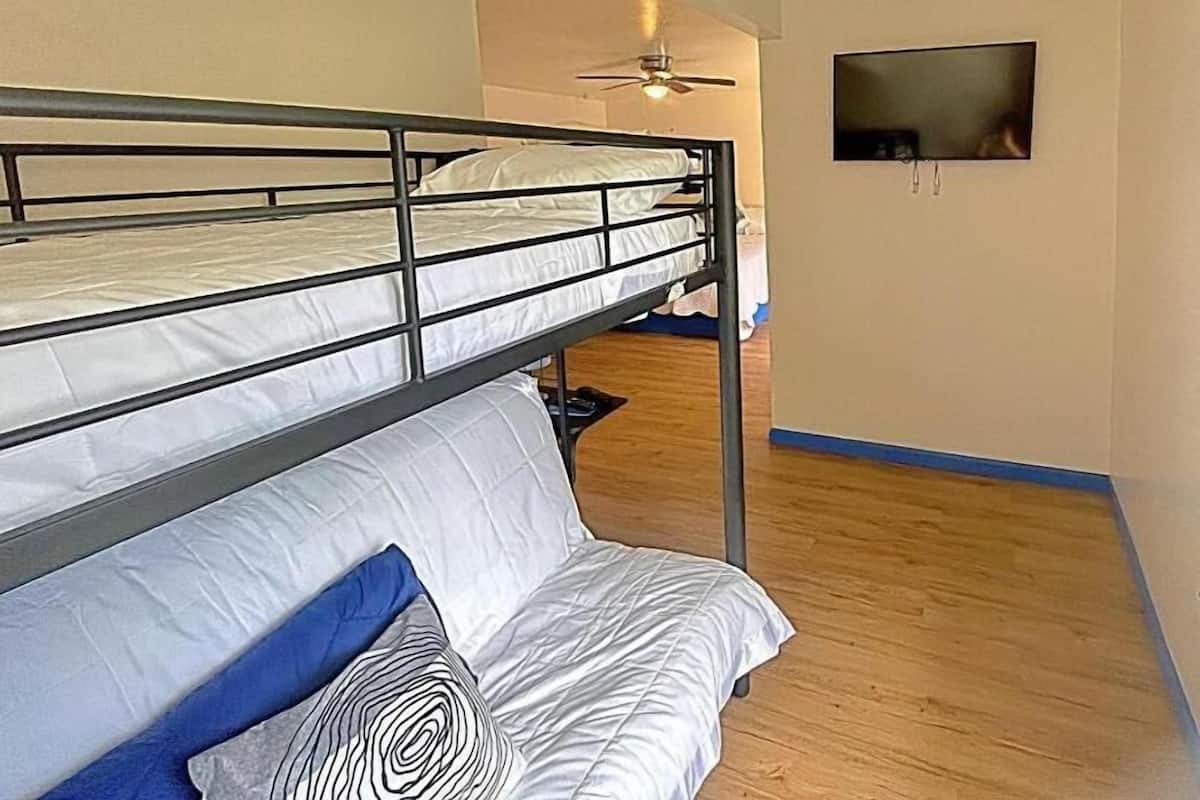 Una habitación con literas, ventilador de techo, televisor y piso de madera.