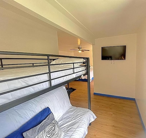 Una habitación con literas, ventilador de techo, televisor y piso de madera.