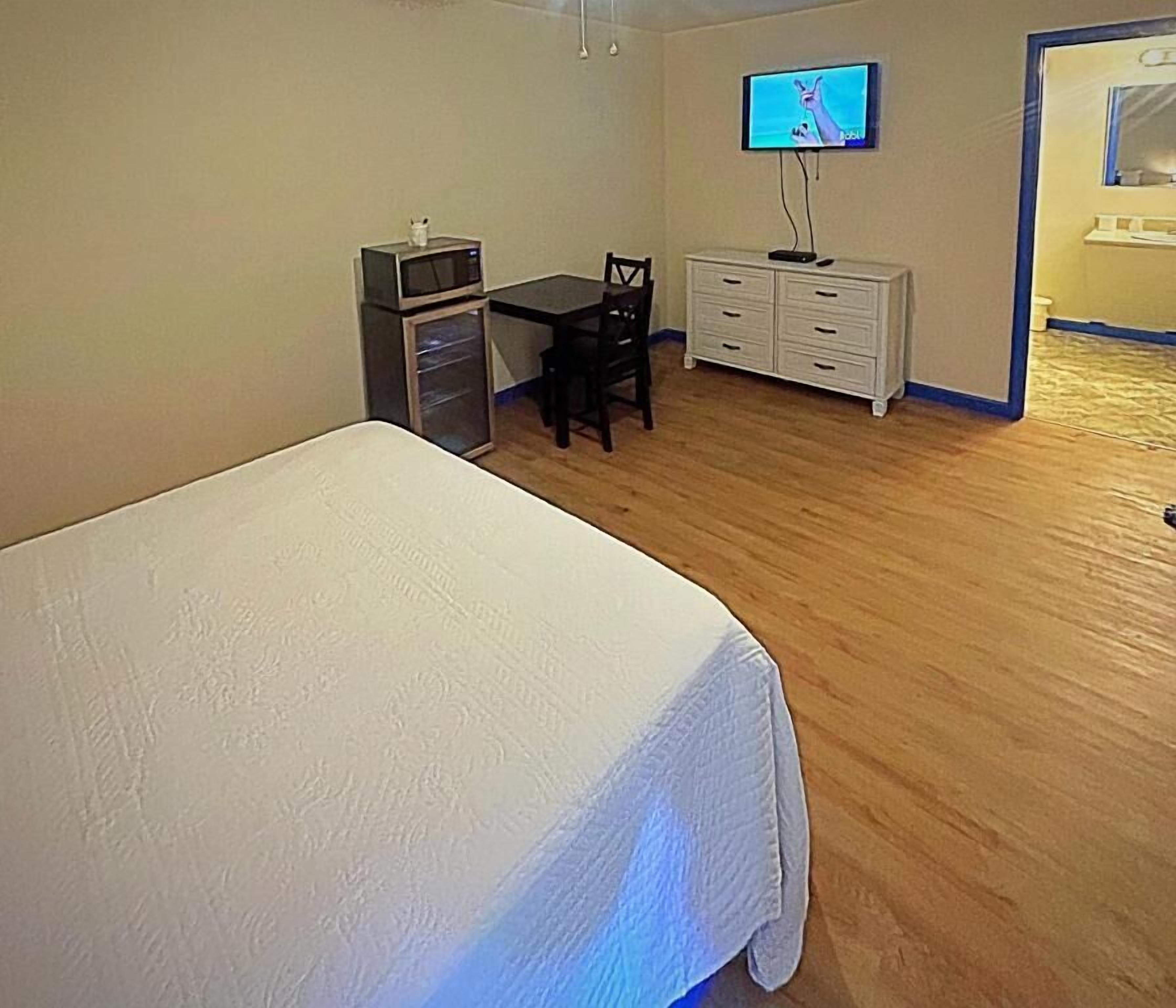 A bedroom with a bed, a desk, a TV, a dresser, and a microwave.
