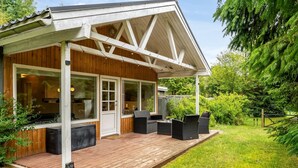 En stuga byggd av tr ä med en inglasad veranda, stora fönster och utemöbler.