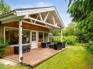 Eine Holzhütte mit überdachter Veranda, großen Fenstern und Sitzgelegenheiten im Freien.