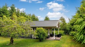 Ett litet hus med en inglasad veranda, omgivet av frodig grönska och träd.