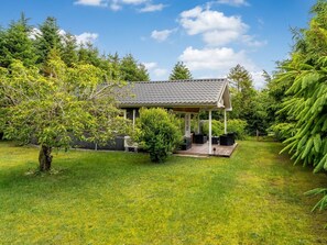 Ein kleines Haus mit überdachter Veranda, umgeben von üppiger Vegetation und Bäumen.