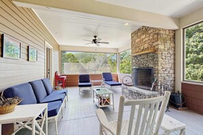 A covered patio with a stone fireplace, seating, and a ceiling fan. - Charming house, mountain views, fireplace, trail access, cable TV, w/d, AC (Montreat)