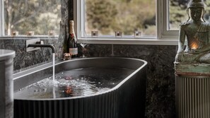 A bathroom with a black bathtub, a faucet, and a statue of a seated figure. - Boatshed Villas by Istana - Green Door, villa by Lake Daylesford (Daylesford)