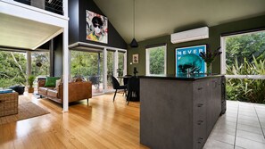 Eine moderne Küche mit einer großen Kochinsel, einem Essbereich mit Sofa und Stühlen sowie großen Fenstern mit Blick auf Grünflächen.