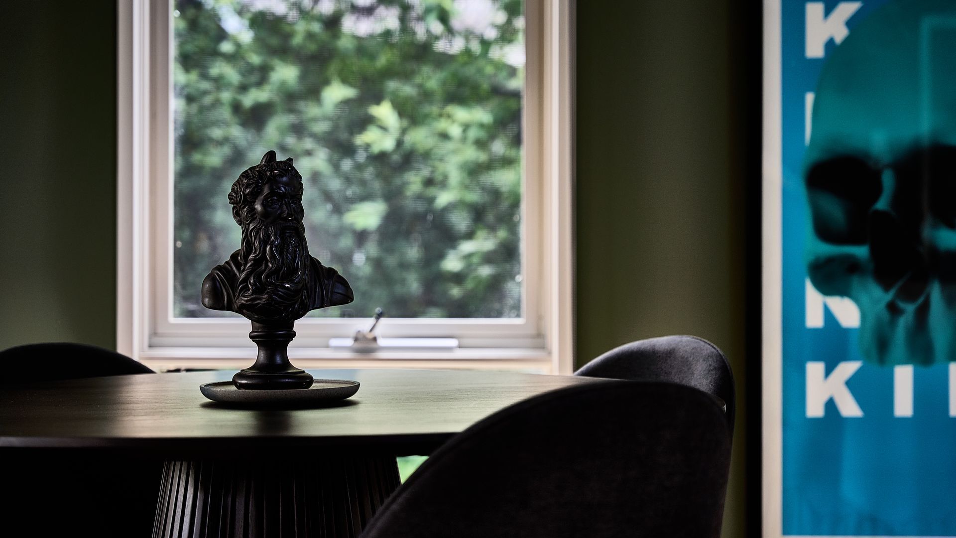 A bust on a table with a window in the background.