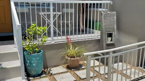 A balcony with a white railing, potted plants, and a small stone structure. - Modern, cozy unit in quiet neighborhood close to EVERYTHING. (Coral Gables)