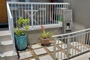 Ein Balkon mit weißer Reling, Blumentöpfen und einer kleinen Steinstruktur.