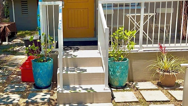 A house with a yellow door, a white railing, and potted plants. - Modern, cozy unit in quiet neighborhood close to EVERYTHING. (Coral Gables)