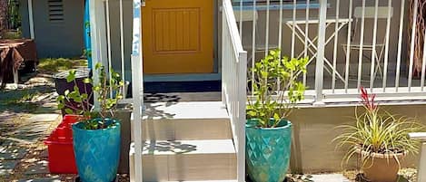 Una casa con puerta amarilla, barandilla blanca y plantas en macetas.