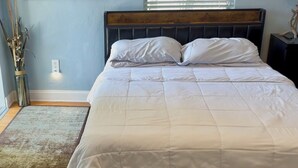 A bed with a wooden headboard, a white quilt, and a vase with dried plants. - Modern, cozy unit in quiet neighborhood close to EVERYTHING. (Coral Gables)