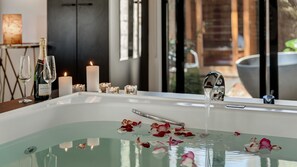 Ein Badezimmer mit einer Badewanne, Kerzen und Rosenblättern.