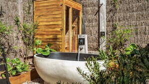 Zona d'spa amb una gran banyera de formigó, una cabana de fusta i diverses plantes.