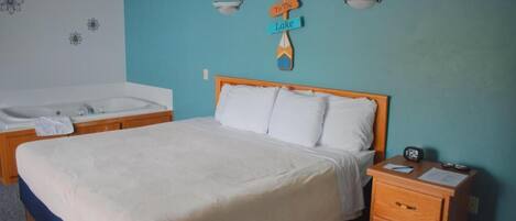 A bedroom with a bed, a nightstand, a wooden headboard, a wall-mounted sign, a bathtub, and a towel.