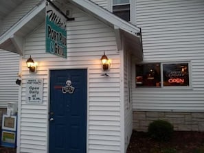 Rakennuksessa on kyltti, jossa lukee ”Mike’s PORT PUB & GRILL”, sininen ovi ja kaksi seinälle asennettua valaisinta.
