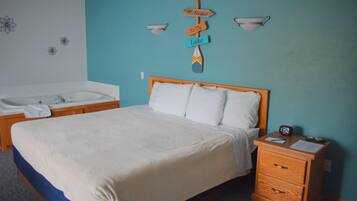 A bedroom with a bed, a nightstand, a wooden headboard, a wall-mounted sign, a bathtub, and a towel.