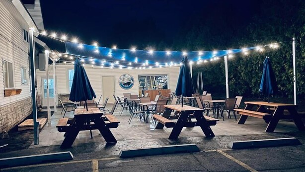 An outdoor patio area with picnic tables and umbrellas, string lights, and a building with a sign in the background. - Innlet Motel (Sturgeon Bay)