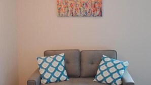 A gray sofa with patterned pillows, a hanging light fixture, and a colorful abstract painting on the wall. - Innlet Motel (Sturgeon Bay)