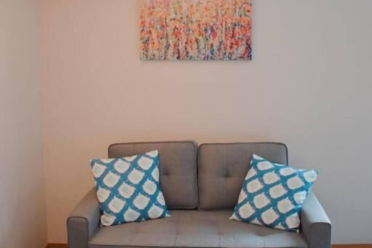 Un sofá gris con almohadones estampados, una lámpara colgante y un cuadro abstracto colorido en la pared.