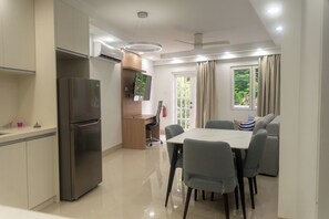 Eine moderne Küche mit integriertem Kühlschrank, ein Essbereich mit Tisch und Stühlen, eine Couch und ein Deckenventilator.