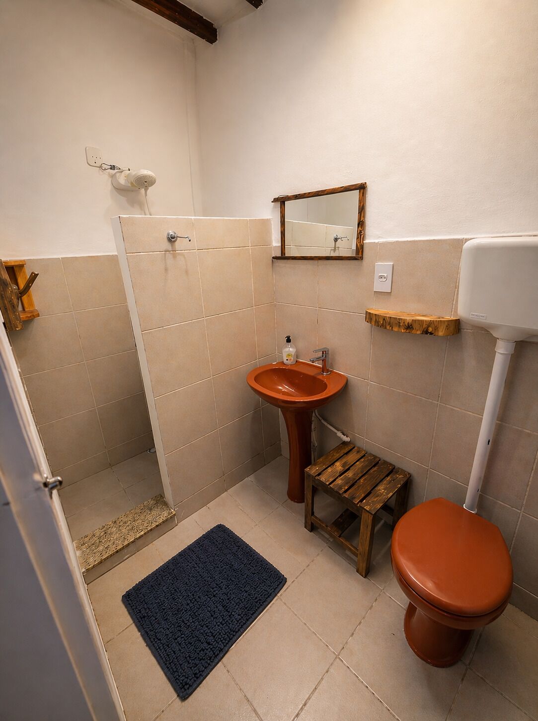 A bathroom with a shower, sink, toilet, and a small wooden stool.