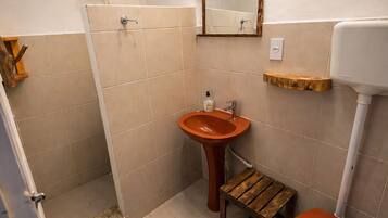 A bathroom with a shower, sink, toilet, and a small wooden stool.