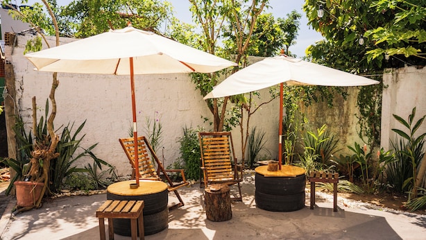 An outdoor seating area with wooden chairs and tables, surrounded by potted plants and trees. - Nossa Casa Itacaré (Itacaré)