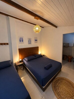 A bedroom with a large bed, a bedside table, a hanging light fixture, and a small bathroom visible through an open door. - Nossa Casa Itacaré (Itacaré)