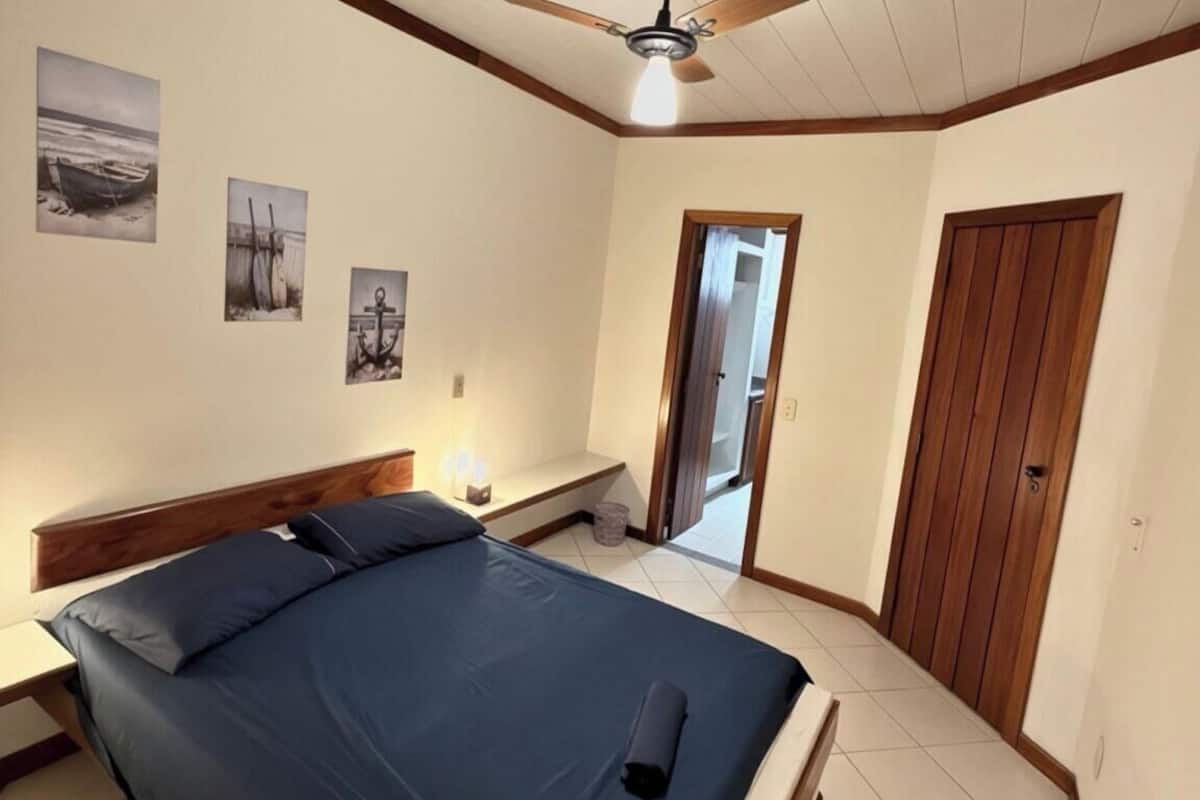 A bedroom with a bed, a ceiling fan, and three wall-mounted pictures.