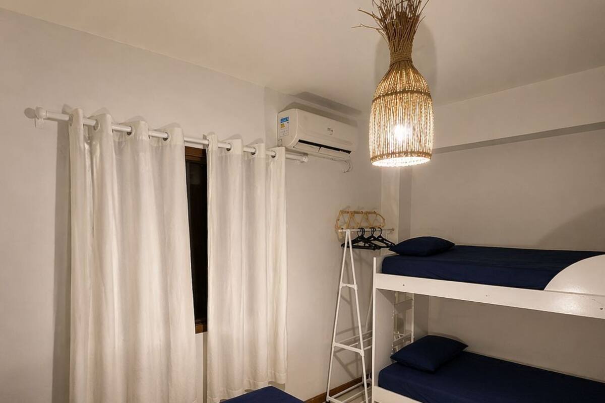 Una habitación con literas, un equipo de aire acondicionado blanco, un estante blanco y una lámpara colgante.