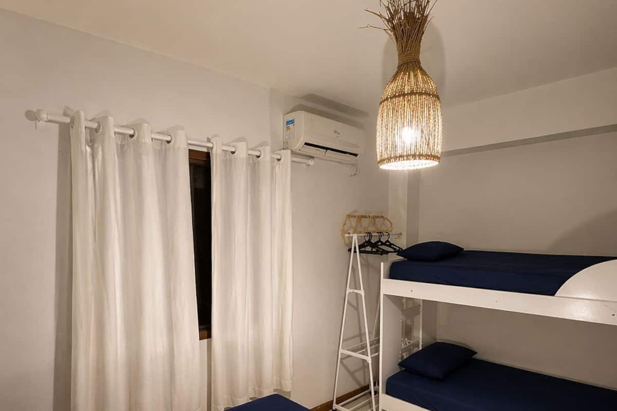 A room with bunk beds, a white air conditioning unit, a white shelf, and a hanging light fixture.