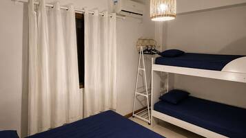 Quarto com beliches, ar-condicionado branco, prateleira branca e luminária pendente.