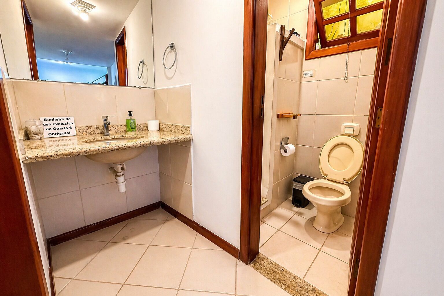 A bathroom with a sink, toilet, and shower. There is a sign on the sink and a wooden door frame.