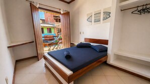 A bedroom with a bed, a wooden headboard, a nightstand, a wardrobe, and a view of a colorful building outside. - Nossa Casa Itacaré (Itacaré)